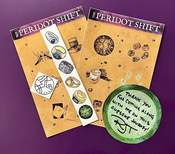on a purple counter, a spread of sticker sheets along with a signed book plate and a temporary tattoo.